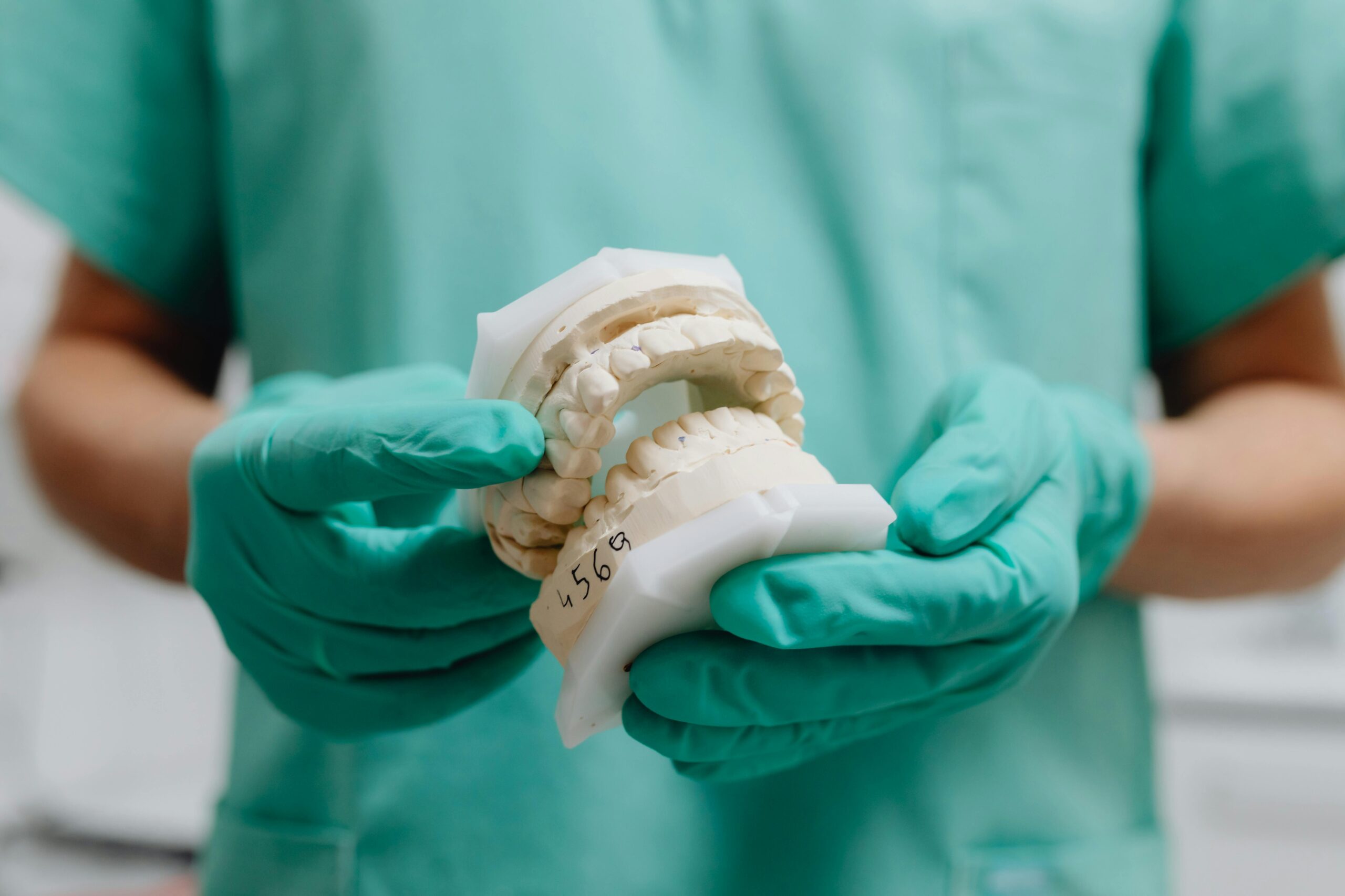 Close-up of a dental professional wearing gloves holding a dental cast model.